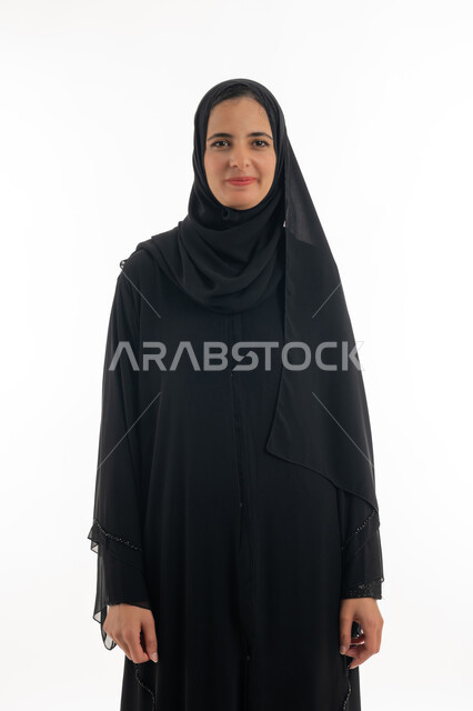 الاهتمام والعنايه بالمظهر الخارجي، بورتريه بالطول الكامل لسيده عربيه خليجيه اماراتيه ترتدي الحجاب والعباءه السوداء تقف وتنظر الى الكاميرا بايماءات الثقه بالنفس، مفهوم الأنوثة والنعومة، خلفية بيضاء
