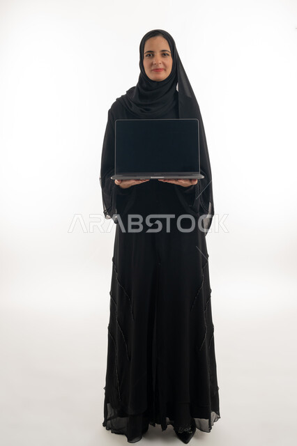 تصفح الانترنت وبرامج التواصل الاجتماعي, إستخدام الحاسوب لإنجاز المهام، بورتريه لسيده عربيه خليجيه اماراتيه ترتدي العباءه والحجاب تحمل بيدها جهاز اللاب توب المحمول، تطور التكنولوجيا والأجهزة التقنية، خلفية بيضاء