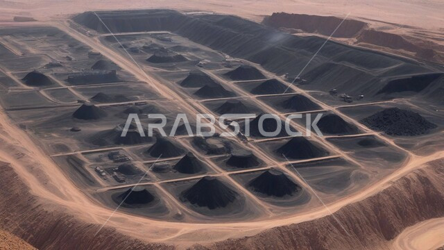 Natural coal mines, areas for prospecting for underground resources, rocky nature and terrain of mountain ranges, highlands and mountain peaks in the Kingdom of Saudi Arabia, a group of large freight vehicles working at the mining site, removing dirt and rocks and transporting them away