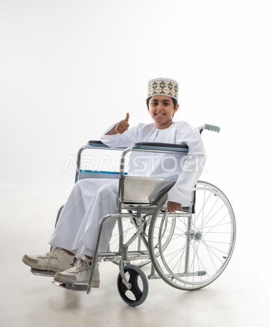 رفع اصبع الابهام للاعلى دليل على الرضى والقبول, الاهتمام بالاطفال من ذوي الاحتياجات الخاصة في سلطنة عمان, تعابير السعادة والسرور والتفاؤل, بورتريه لطفل عربي خليجي عماني يرتدي الدشداشة و الكمه يجلس على كرسي متحرك, خلفية بيضاء
