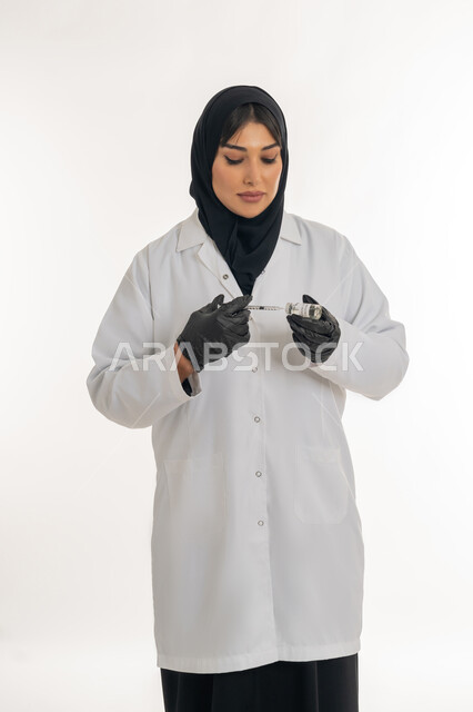 التطعيم ضد الفايروسات، الحفاظ على السلامة والحماية من الامراض، الوعي الصحي وتجنب إنتشار العدوى، بورتريه لطبيبة عربية خليجة اماراتية محجبة ترتدي المعطف الطبي تحمل بيدها الحقنة تقوم بتجهيز لقاح كورونا (كوفيد -19 )، شابة سعودية تتبع اجراءات الوقاية، خلفية بيضاء