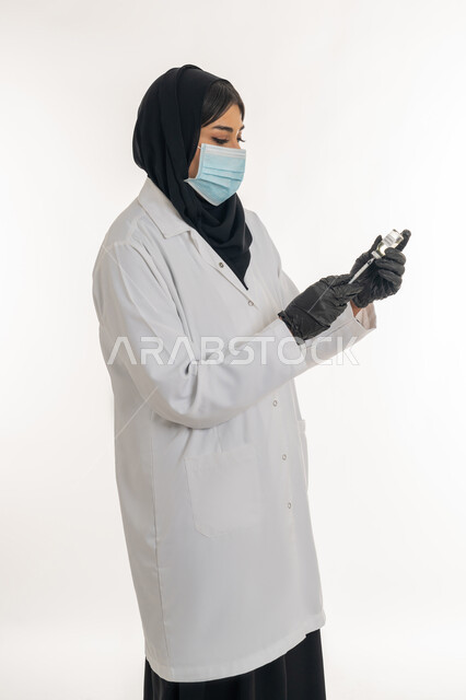 تجنب إنتشار العدوى، الحفاظ على السلامة والحماية من الامراض، مفهوم الوعي الصحي، بورتريه من الجانب لطبيبة عربية خليجة اماراتية محجبة ترتدي المعطف الطبي تحمل بيدها الحقنة تقوم بتجهيز لقاح كورونا (كوفيد -19 )، شابة سعودية تتبع اجراءات الوقاية، خلفية بيضاء