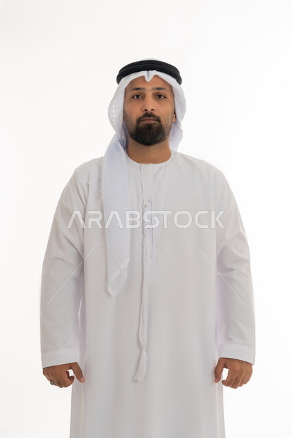تعابير الجدية والحزم، مفهوم الاناقة والرجولة، الاهتمام بالمظهر الخارجي، بورتريه لرجل عربي خليجي اماراتي يرتدي الكندورة والغترة البيضاء يقف باستقامة ينظر إلى الكاميرا بايماءات الثقة بالنفس، خلفية بيضاء
