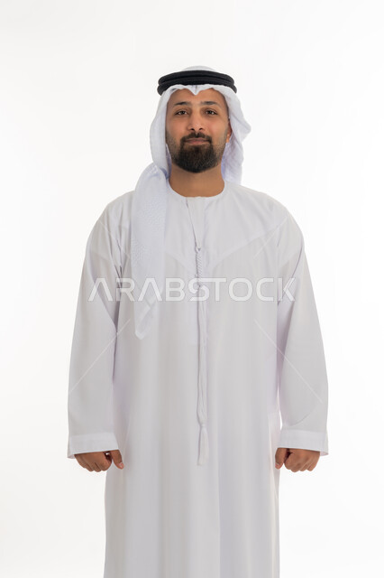 مفهوم الاناقة والرجولة، تعابير الجدية والحزم، الإهتمام بالمظهر الخارجي، بورتريه لرجل عربي خليجي اماراتي يرتدي الكندورة والغترة البيضاء يقف باستقامة ينظر إلى الكاميرا بايماءات الثقة بالنفس، خلفية بيضاء