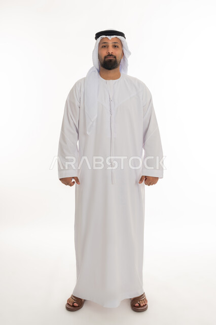 الاهتمام بالمظهر الخارجي، تعابير الجدية والحزم، مفهوم الاناقة والرجولة، بورتريه لرجل عربي خليجي اماراتي يرتدي الكندورة والغترة البيضاء يقف باستقامة ينظر إلى الكاميرا بايماءات الثقة بالنفس، صورة لكامل الجسم، خلفية بيضاء