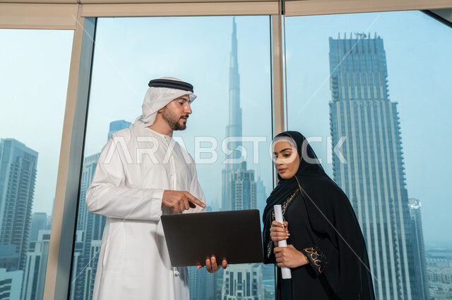 Using the tablet to explain the processes followed, understanding and cooperation between colleagues to achieve the company's goals, professionalism and dedication to achievement, an Arab Gulf Emirati man wearing a white kandura and ghutra holding a tablet in his hand explaining the work plan to his colleague, ensuring a clear and comprehensive understanding of the work
