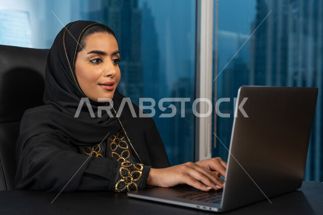 Data entry through the keyboard, the development of technology and the use of modern technical devices, a close-up image of the hands of an Arab Gulf Emirati woman wearing a black abaya, managing business through a laptop, browsing the Internet and social networking programs