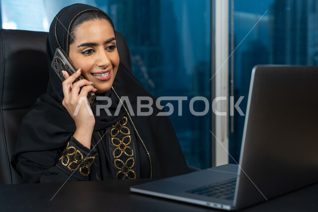 ادارة الأعمال من خلال جهاز الحاسوب المحمول, تصفح الانترنت وبرامج التواصل الاجتماعي, تطور التكنولوجيا وإستخدام الأجهزة التقنية الحديثة, صورة لامرأة عربية خليجية اماراتية محجبة ترتدي العباءة السوداء تقوم بإجراء مكالمة هاتفية عبر الجوال