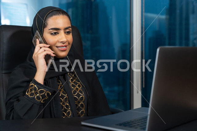 ادارة الأعمال من خلال جهاز الحاسوب المحمول, تصفح الانترنت وبرامج التواصل الاجتماعي, تطور التكنولوجيا وإستخدام الأجهزة التقنية الحديثة, صورة لامرأة عربية خليجية اماراتية محجبة ترتدي العباءة السوداء تقوم بإجراء مكالمة هاتفية عبر الجوال