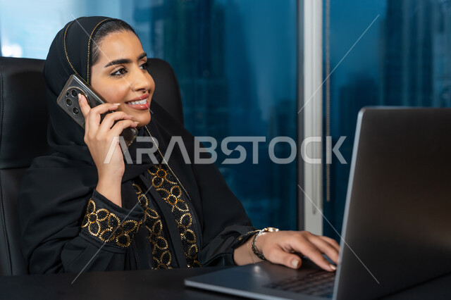 ادارة الأعمال من خلال جهاز الحاسوب المحمول, تصفح الانترنت وبرامج التواصل الاجتماعي, تطور التكنولوجيا وإستخدام الأجهزة التقنية الحديثة, صورة لامرأة عربية خليجية اماراتية محجبة ترتدي العباءة السوداء تقوم بإجراء مكالمة هاتفية عبر الجوال