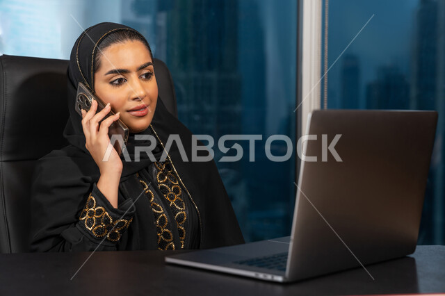 ادارة الأعمال من خلال جهاز الحاسوب المحمول, تصفح الانترنت وبرامج التواصل الاجتماعي, تطور التكنولوجيا وإستخدام الأجهزة التقنية الحديثة, صورة لامرأة عربية خليجية اماراتية محجبة ترتدي العباءة السوداء تقوم بإجراء مكالمة هاتفية عبر الجوال