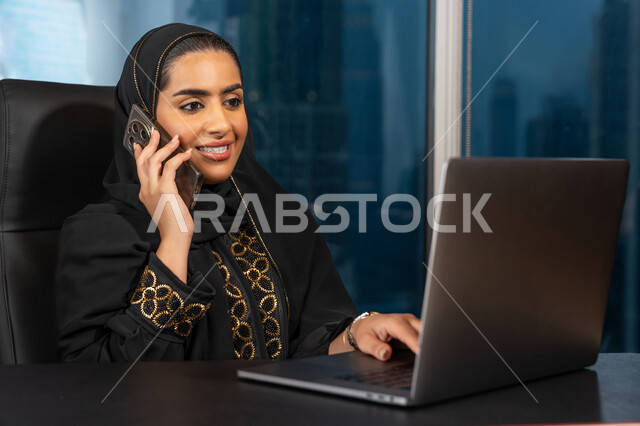 ادارة الأعمال من خلال جهاز الحاسوب المحمول, تصفح الانترنت وبرامج التواصل الاجتماعي, تطور التكنولوجيا وإستخدام الأجهزة التقنية الحديثة, صورة لامرأة عربية خليجية اماراتية محجبة ترتدي العباءة السوداء تقوم بإجراء مكالمة هاتفية عبر الجوال