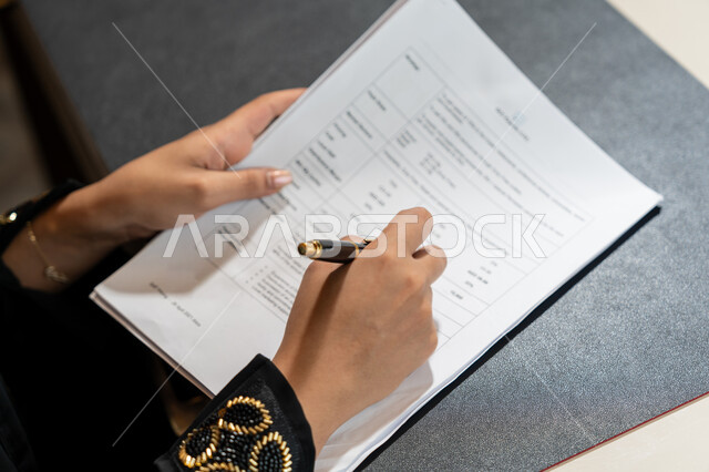 تنظيم وإدارة الأعمال, تدوين وتسجيل الملاحظات والمعلومات على الورق, صورة مقربة ليدين امرأة عربية خليجية اماراتية ترتدي العباءة السوداء تقوم بكتابة المهام والأهداف اليومية