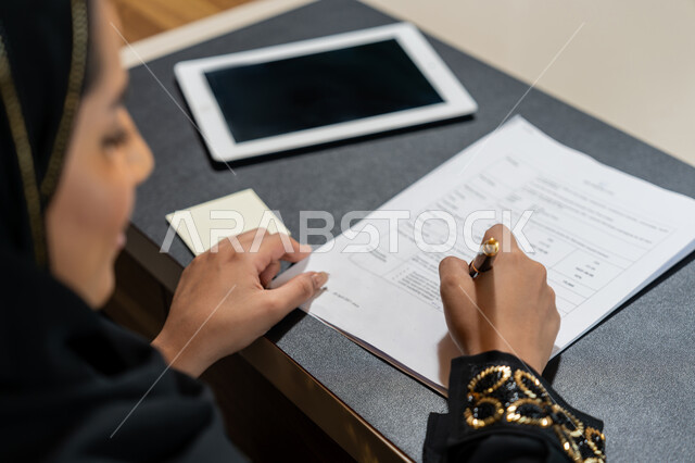 تنظيم وإدارة الأعمال, تدوين وتسجيل الملاحظات والمعلومات على الورق, صورة مقربة ليدين امرأة عربية خليجية اماراتية ترتدي العباءة السوداء تقوم بكتابة المهام والأهداف اليومية