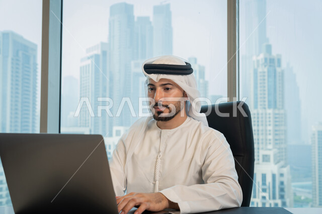 مهن ووظائف ادارية مكتبية, تصفح الانترنت وبرامج التواصل الاجتماعي, تطور التكنولوجيا وإستخدام الأجهزة التقنية الحديثة, صورة لرجل عربي خليجي اماراتي يرتدي الزي التقليدي ويقوم بادارة الأعمال من خلال جهاز الحاسوب المحمول