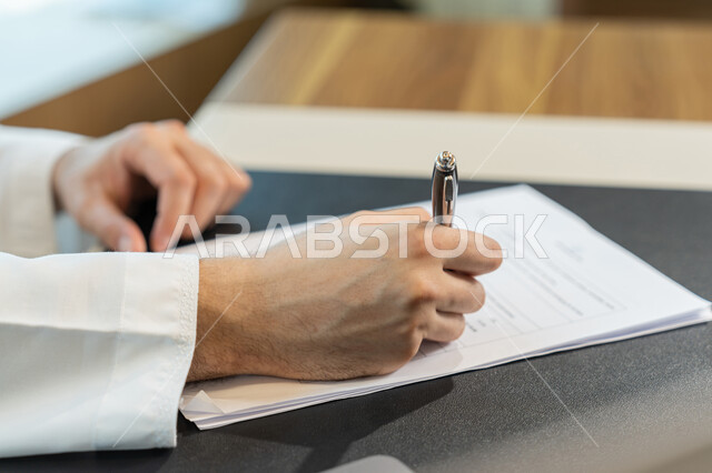 تنظيم وإدارة الأعمال، تدوين وتسجيل الملاحظات والمعلومات على الورق, صورة مقربة ليدين شاب عربي خليجي اماراتي يرتدي الثوب التقليدي يقوم بكتابة المهام والأهداف اليومية