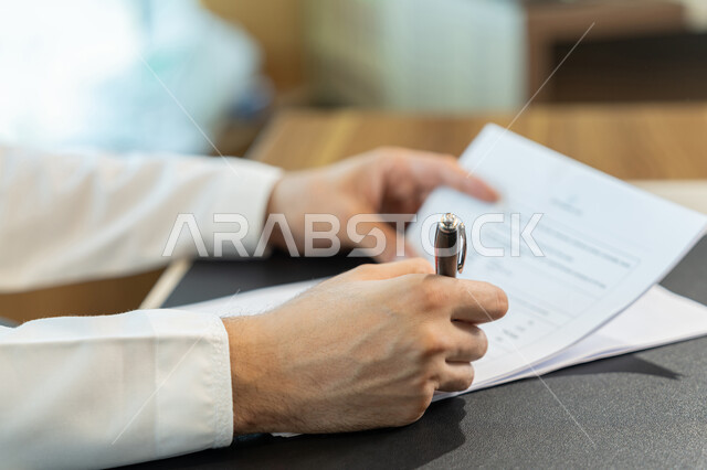 إدارة الأعمال وتنظيمها، تدوين وتسجيل الملاحظات والمعلومات على الورق, صورة مقربة ليدين شاب عربي خليجي اماراتي يرتدي الثوب التقليدي يقوم بكتابة المهام والأهداف اليومية