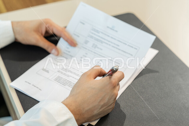 تنظيم وإدارة الأعمال، تدوين وتسجيل الملاحظات والمعلومات على الورق, صورة مقربة ليدين شاب عربي خليجي اماراتي يرتدي الثوب التقليدي يقوم بكتابة المهام والأهداف اليومية