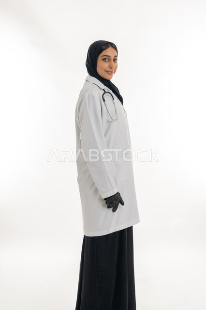 مهن ووظائف نسائية, تقديم المساعده الطبية للمرضى, شابة سعودية تقوم بالعمل في المراكز والمستشفيات, بورتريه لطبيبة عربية خليجية اماراتية ترتدي المعطف الطبي الأبيض وسماعة الفحص تنظر إلى الكاميرا بايماءات الثقة بالنفس, مفهوم الطب والرعاية الصحية, خلفية بيضاء