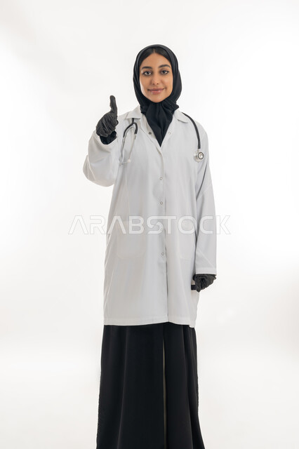 The concept of medicine and health care, working in health centers and hospitals, providing medical assistance to patients, a portrait of a veiled female Emirati Gulf Arab doctor wearing a white medical coat and an examination stethoscope with hand gestures indicating admiration, white background