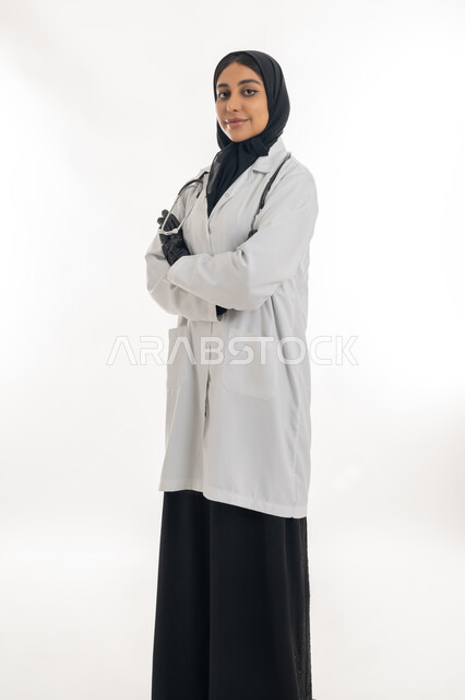 العمل في المراكز الصحية والمستشفيات، تقديم المساعده الطبية للمرضى, طبيبة عربية خليجية سعودية محجبة ترتدي المعطف الطبي الأبيض وسماعة الفحص, بورتريه لشابة إماراتية تعمل في المجال الطبي، مفهوم الطب والرعاية الصحية, خلفية بيضاء