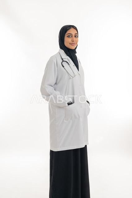 مهن ووظائف نسائية, تقديم المساعده الطبية للمرضى, شابة سعودية تقوم بالعمل في المراكز والمستشفيات, بورتريه لطبيبة عربية خليجية اماراتية ترتدي المعطف الطبي الأبيض وسماعة الفحص تنظر إلى الكاميرا بايماءات الثقة بالنفس, مفهوم الطب والرعاية الصحية, خلفية بيضاء