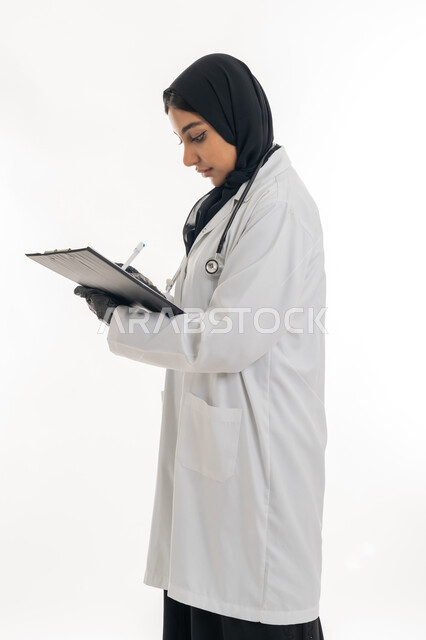 العمل في القطاع الصحي, مفهوم الأنوثة والنعومة، تقديم المساعده الطبية للمرضى, بورتريه لطبيبة عربية خليجية اماراتية محجبة ترتدي المعطف الطبي الأبيض تقوم بإعداد التقارير الطبية, تشخيص الحالات المرضية, خلفية بيضاء