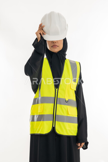 مفهوم الهندسة وأعمال البناء, مهن ووظائف نسائية، تقدم وتطور الامارات على يد أبناء الوطن، شابة سعودية تمسك بيدها خوذة الحماية، بورتريه لمهندسة عربية خليجية اماراتية محجبة ترتدي عباءة سوداء مع السترة تعمل في القطاع الهندسي الاماراتي, خلفية بيضاء