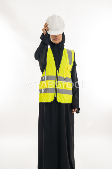 مفهوم الهندسة وأعمال البناء, مهن ووظائف نسائية، تقدم وتطور الامارات على يد أبناء الوطن، شابة سعودية تمسك بيدها خوذة الحماية، بورتريه لمهندسة عربية خليجية اماراتية محجبة ترتدي عباءة سوداء مع السترة تعمل في القطاع الهندسي الاماراتي, خلفية بيضاء