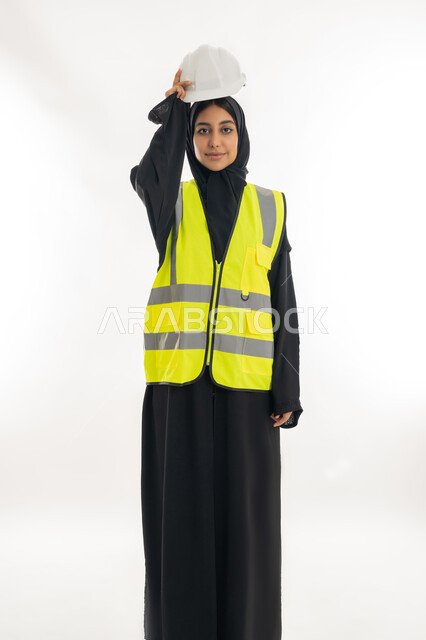 The concept of engineering and construction work, women's professions and jobs, the progress and development of the Emirates at the hands of the sons of the homeland, a young Saudi woman holding a protective helmet in her hand, a portrait of a veiled Arab Gulf Emirati female engineer wearing a black abaya with a jacket working in the Emirati engineering sector, white background