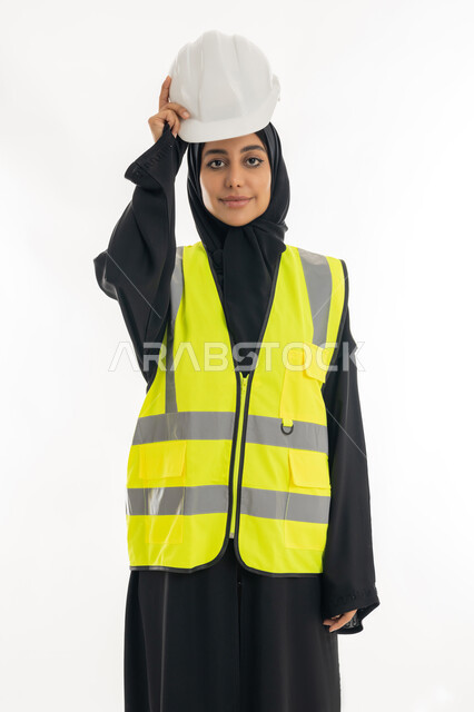 The concept of engineering and construction work, women's professions and jobs, the progress and development of the Emirates at the hands of the sons of the homeland, a young Saudi woman holding a protective helmet in her hand, a portrait of a veiled Arab Gulf Emirati female engineer wearing a black abaya with a jacket working in the Emirati engineering sector, white background