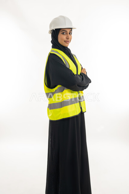 مفهوم ادارة المشاريع الهندسية,  وظائف ومهن نسائية, العمل في القطاع الهندسي, الوقوف بايماءات الثقة,  بورتريه لمهندسة معمارية عربية خليجية امارتية ترتدي خوذة الحماية و السترة وتقف بايدي متقاطعة، خلفية بيضاء