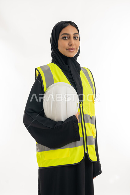 مفهوم الهندسة وأعمال البناء, مهن ووظائف نسائية، تقدم وتطور الامارات على يد أبناء الوطن، شابة سعودية تمسك بيدها خوذة الحماية، بورتريه لمهندسة عربية خليجية اماراتية محجبة ترتدي عباءة سوداء مع السترة تعمل في القطاع الهندسي الاماراتي, خلفية بيضاء