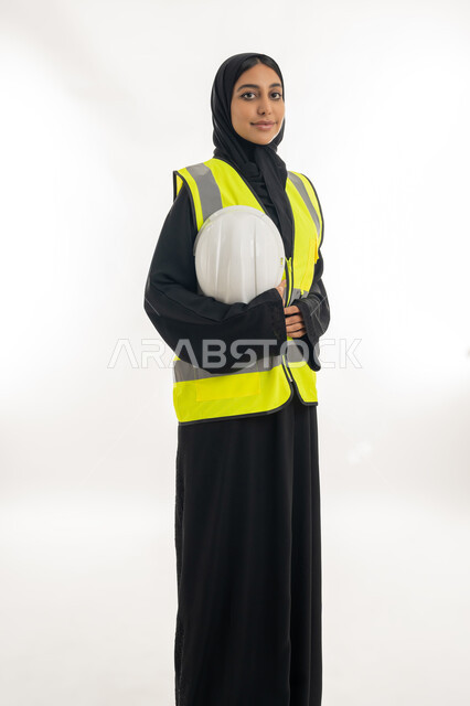 مفهوم الهندسة وأعمال البناء, مهن ووظائف نسائية، تقدم وتطور الامارات على يد أبناء الوطن، شابة سعودية تمسك بيدها خوذة الحماية، بورتريه لمهندسة عربية خليجية اماراتية محجبة ترتدي عباءة سوداء مع السترة تعمل في القطاع الهندسي الاماراتي, خلفية بيضاء