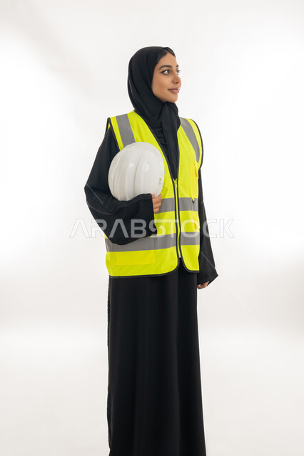 مفهوم الهندسة وأعمال البناء, مهن ووظائف نسائية، تقدم وتطور الامارات على يد أبناء الوطن، شابة سعودية تمسك بيدها خوذة الحماية، بورتريه لمهندسة عربية خليجية اماراتية محجبة ترتدي عباءة سوداء مع السترة تعمل في القطاع الهندسي الاماراتي, خلفية بيضاء