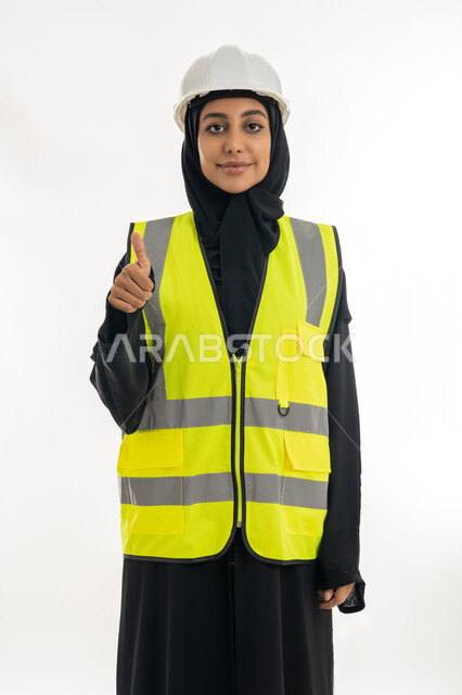 علامة الجودة و الامتياز، تقدم وتطور الامارات على يد أبناء الوطن، مفهوم الهندسة وأعمال البناء, شابة سعودية ترفع اصبع الابهام للاعلى بايماءات الموافقة، بورتريه لمهندسة عربية خليجية اماراتية محجبة ترتدي السترة وخوذة الحماية تعمل في القطاع الهندسي, خلفية بيضاء