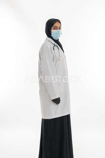 العمل في القطاع الصحي الاماراتي, مهن ووظائف نسائية، شابة سعودية تقدم الرعاية الطبية للمرضى، بورتريه لطبيبة عربية خليجية اماراتية محجبة ترتدي العباءة السوداء مع المعطف الطبي الأبيض وكمامة الوقاية، الالتزام بالاحترازات الوقائيه ضد كوفيد 19، خلفية بيضاء