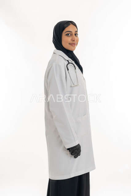 مهن ووظائف نسائية, تقديم المساعده الطبية للمرضى, شابة سعودية تقوم بالعمل في المراكز والمستشفيات, بورتريه من الجانب لطبيبة عربية خليجية اماراتية ترتدي المعطف الطبي الأبيض وسماعة الفحص تنظر إلى الكاميرا بايماءات الثقة بالنفس, مفهوم الطب والرعاية الصحية, خلفية بيضاء