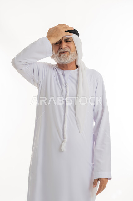 Hand on head with expression of suddenly remembering something, gestures of disappointment and suffering with forgetfulness, close-up portrait of elderly Emirati Gulf Arab man wearing traditional Emirati kandura and ghutra standing and feeling upset, white background
