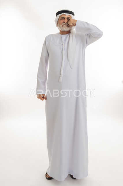 حركات وجه ويدين مختلفة تدل على الانزعاج والشعور بالاضطراب، بورتريه لرجل عربي خليجي إماراتي كبير بالسن يرتدي الكندورة الإماراتية التقليدية والغترة يضع قبضته على وجهه بإيماءات التألم وعدم الارتياح، الجسم بالطول الكامل، خلفية بيضاء