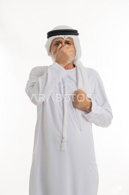 إشارات وحركات وجه ويدين مختلفة تدل على التألم والإحساس بالمرض، النظر إلى الكاميرا والشعور بالاضطراب والتعب، بورتريه مقرب لرجل عربي خليجي إماراتي كبير بالسن يرتدي الكندورة الإماراتية التقليدية والغترة يغطي وجهه بيده بإيماءات الحزن، خلفية بيضاء