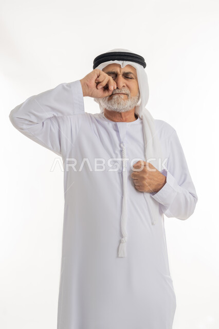 الشعور بالاضطراب والتعب، إشارات وحركات وجه ويدين مختلفة تدل على الانزعاج وعدم الرضا، بورتريه مقرب لرجل عربي خليجي إماراتي كبير بالسن يرتدي الكندورة الإماراتية التقليدية والغترة يضع قبضته على وجهه بإيماءات التألم، خلفية بيضاء