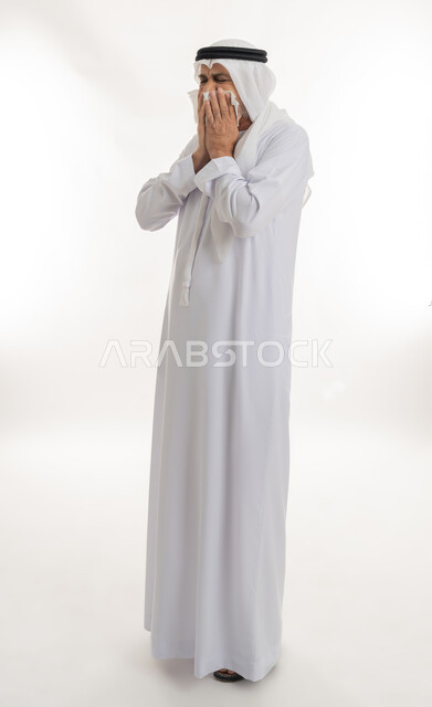 الإصابة بالانفلونزا والعطاس والإحساس بأعراض الزكام، إيماءات الألم والتعب والمرض, بورتريه من الجانب لرجل كبير السن عربي خليجي اماراتي يرتدي الغترة والكندورة يمسك المنديل بيديه ويغطي أنفه، الحاجة للراحة وأخذ العلاج المناسب, الجسم بالطول الكامل، خلفية بيضاء