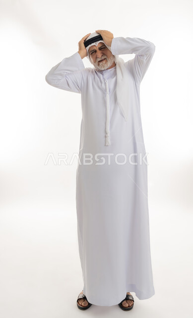 الشعور بالدوار وإيماءات التعب والمرض, الإحساس بوجع الرأس و الدوخة, آلام الشقيقة والصداع النصفي ,بورتريه لرجل كبير السن عربي خليجي اماراتي يرتدي الغترة والكندورة يمسك رأسه بيديه ويشعر بالألم, الحاجة للعلاج والراحة، الجسم بالطول الكامل، خلفية بيضاء