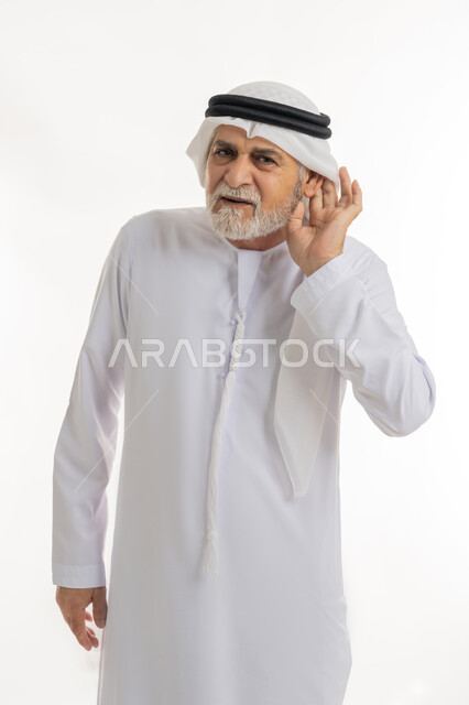 إيماءات التركيز والاستماع لفهم الكلام بشكل واضح، الحاجة لمراجعة طبيب الأذن لتركيب السماعات الطبية, بورتريه مقرب لرجل كبير السن عربي خليجي إماراتي يرتدي الغترة والكندورة يمسك أذنه بيده ويعاني من ضعف السمع، خلفية بيضاء