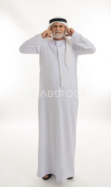 الحاجة إلى الهدوء والسكون، إيماءات الاضطراب والانزعاج من الصوت العالي, بورتريه لرجل كبير السن عربي خليجي إماراتي يرتدي الغترة والكندورة يغلق أذنيه بأصابعه للتخفيف من الضجيج المحيط به، الجسم بالطول الكامل، خلفية بيضاء
