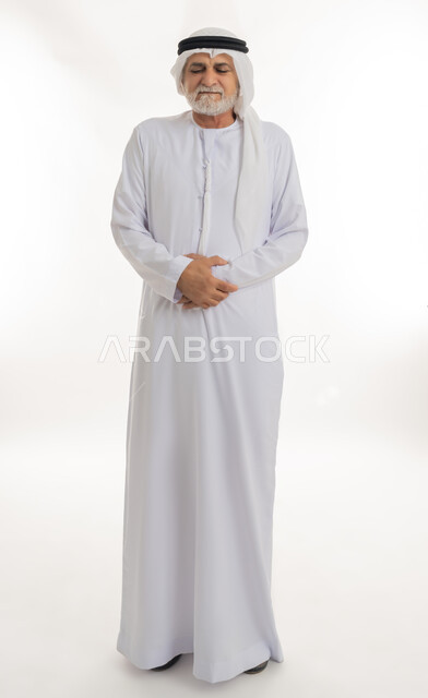 الشعور بالمرض ووجع في البطن, حركات وجه ويدين تدل على الاضطراب والانزعاج، ضرورة الراحة وأخذ العلاج المناسب، بورتريه لرجل كبير السن عربي خليجي إماراتي يرتدي الغترة والكندورة يضع يديه على بطنه بتعابير التألم, الجسم بالطول الكامل، خلفية بيضاء