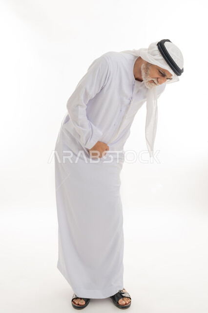 ضرورة الراحة وأخذ العلاج المناسب، الشعور بالمرض ووجع في البطن, بورتريه لرجل كبير السن عربي خليجي إماراتي يرتدي الغترة والكندورة يضع يديه على بطنه بتعابير التألم, الانطواء على النفس من شدة الألم والتعب، الجسم بالطول الكامل، خلفية بيضاء