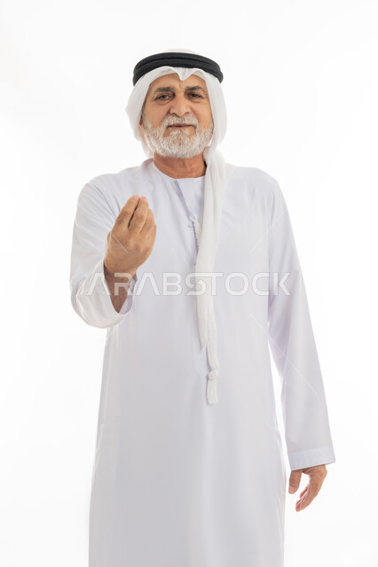 حركات وجه ويدين تدل على التروي والصبر, بورتريه مقرب لرجل كبير بالسن عربي خليجي إماراتي يرتدي الغترة والكندورة يرفع قبضته بإيماءات التمهل والانتظار، الوقوف والنظر إلى الكاميرا بتعابير البشاشة، خلفية بيضاء