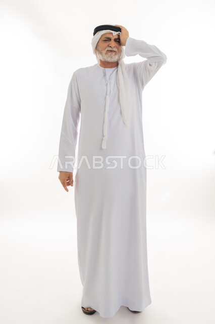 Feeling headache and dizziness, migraine pain, gestures of pain, fatigue and illness, portrait of an elderly Arab Gulf Emirati man wearing a ghutra and kandura, putting his hands on his head feeling dizzy, need for treatment and rest, full body, white background